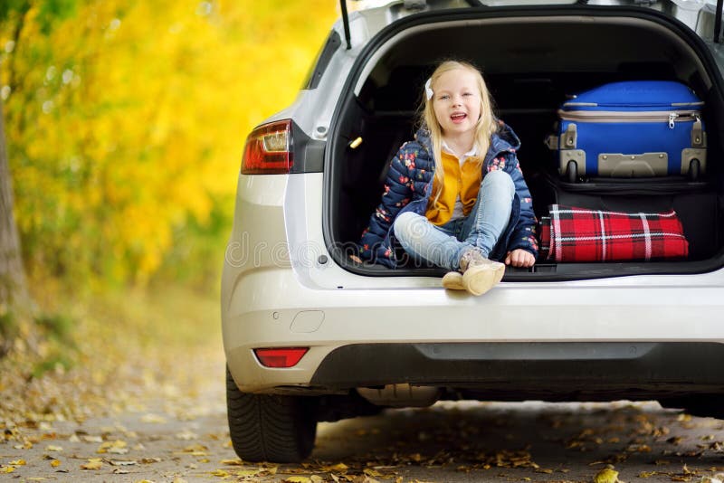 Adorable girl sitting ain a car trunk ready to go on vacations with her parents. Child looking forward for a road trip or travel. Autumn break at school. Traveling by car with kids. Adorable girl sitting ain a car trunk ready to go on vacations with her parents. Child looking forward for a road trip or travel. Autumn break at school. Traveling by car with kids.