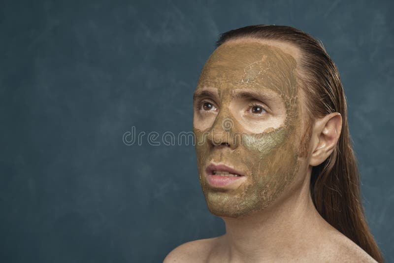 Attentively looking man with wet long hair in green clay mask on his face waiting of the spa procedures. Attentively looking man with wet long hair in green clay mask on his face waiting of the spa procedures