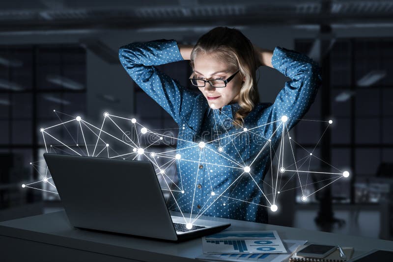 Aantrekkelijk blonde die glazen in donker bureau dragen die laptop met behulp van Gemengde media stock afbeelding Aantrekkelijk blonde die glazen in donker bureau dragen die laptop met behulp van Gemengde media stock afbeelding