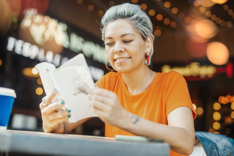 Aantrekkelijk het glimlachen de lezingsboek van het blondemeisje bij koffie en opzij het kijken stock afbeelding Aantrekkelijk het glimlachen de lezingsboek van het blondemeisje bij koffie en opzij het kijken stock afbeelding