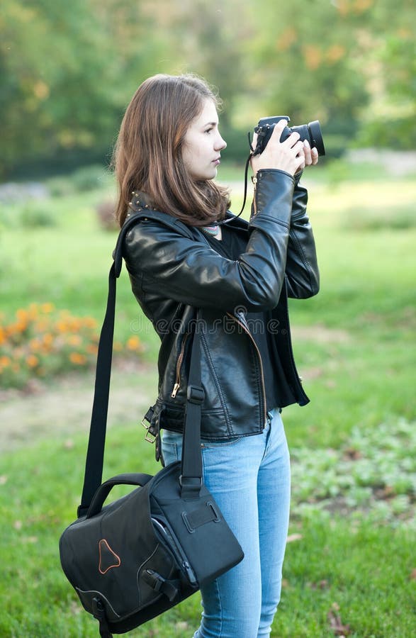 Aantrekkelijk jong meisje die beelden in openlucht nemen Leuke tiener in jeans en zwart leerjasje die foto's in park nemen stock fotografie Aantrekkelijk jong meisje die beelden in openlucht nemen Leuke tiener in jeans en zwart leerjasje die foto's in park nemen stock fotografie