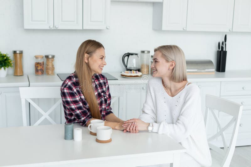 Aantrekkelijk lesbisch wijfje twee die in vrijetijdskleding samen bij de lijst in de keuken zitten, die elkaar bekijken stock foto's Aantrekkelijk lesbisch wijfje twee die in vrijetijdskleding samen bij de lijst in de keuken zitten, die elkaar bekijken stock foto's
