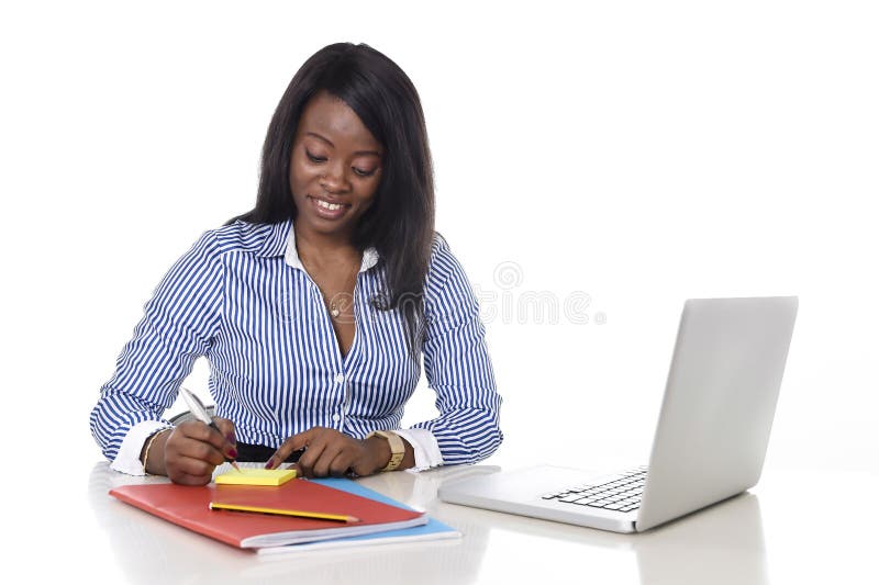 Aantrekkelijke en efficiënte zwarte het behoren tot een bepaald rasvrouw die op blocnote bij laptop van de bureaucomputer bureau