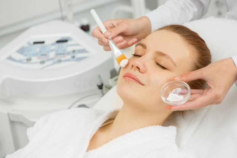 Close up of a happy red haired young woman smiling enjoying facial mask treatment at the beauty salon. Female client getting skincare masks at spa center. Close up of a happy red haired young woman smiling enjoying facial mask treatment at the beauty salon. Female client getting skincare masks at spa center