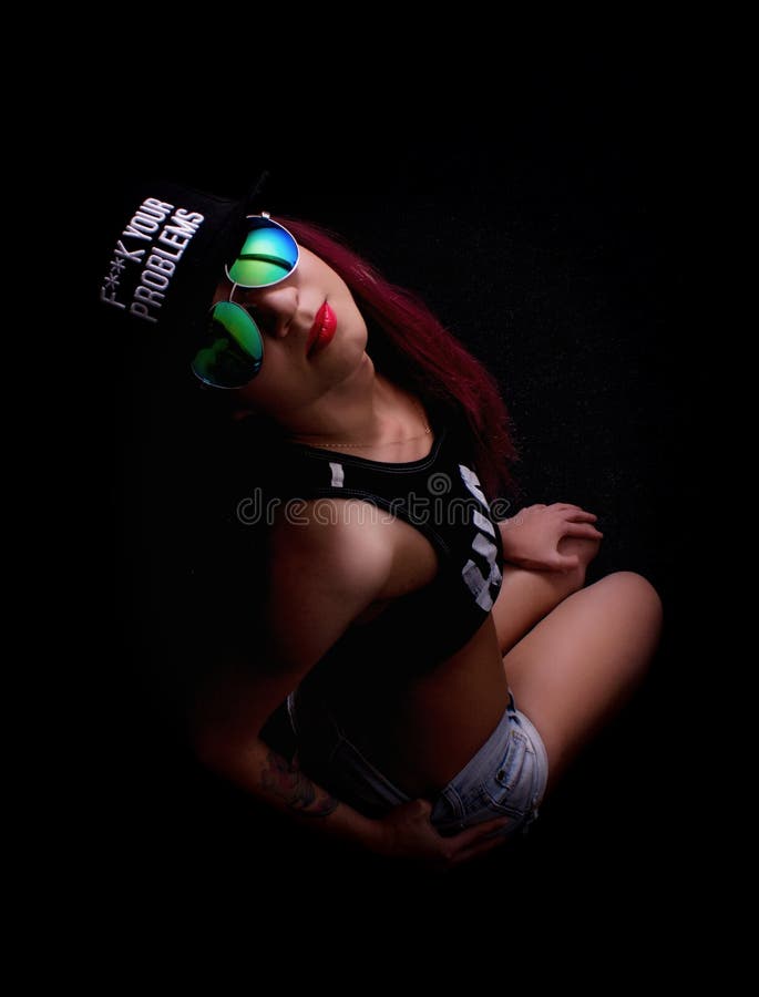 Attractive young woman in cap and sunglasses, smokes on a dark background. Be trendy, be rapper. Attractive young woman in cap and sunglasses, smokes on a dark background. Be trendy, be rapper.