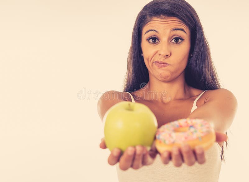 Aantrekkelijke jonge vrouw op een dieet die tussen een appel en een doughnut beslissen stock foto's Aantrekkelijke jonge vrouw op een dieet die tussen een appel en een doughnut beslissen stock foto's