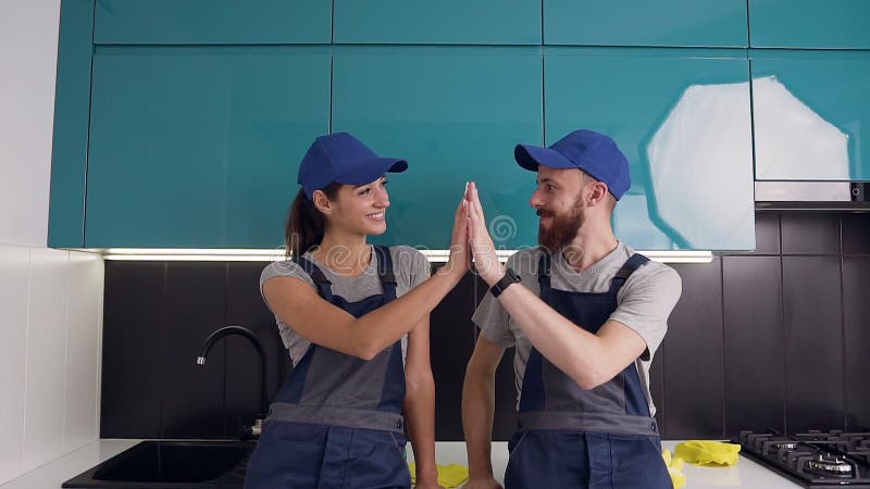 Aantrekkelijke jonge werknemers van de schoonmaakdienst die vijf na goed gedaan werk in de comfortabele keuken leveren