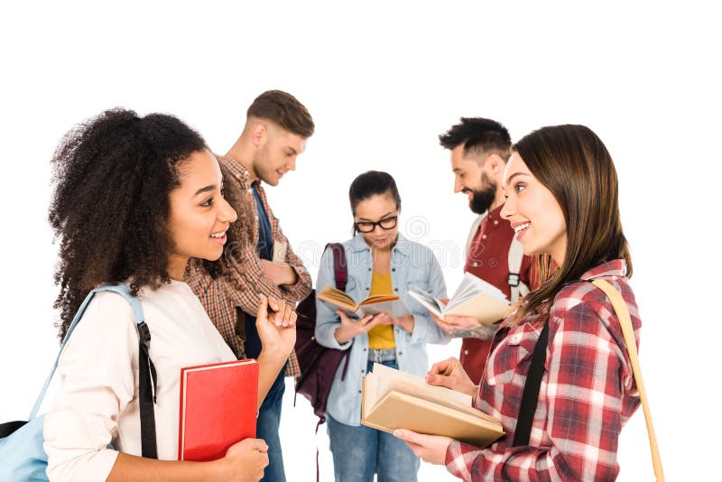 aantrekkelijke multi-etnische meisjes die met boeken in handen dichtbij groep geïsoleerde jongeren spreken stock foto aantrekkelijke multi-etnische meisjes die met boeken in handen dichtbij groep geïsoleerde jongeren spreken stock foto