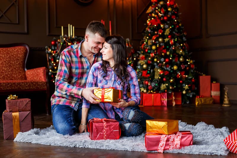 Aantrekkelijke vrolijke man en vrouwenzitting dichtbij Kerstmisboom het koesteren paar geknuffel dichtbij Kerstmisboom stock fotografie Aantrekkelijke vrolijke man en vrouwenzitting dichtbij Kerstmisboom het koesteren paar geknuffel dichtbij Kerstmisboom stock fotografie