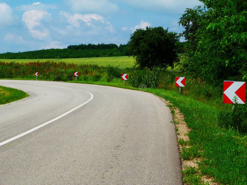Aasfaltweg op het platteland met een scherpe curve en rode en witte zijpijlen op de weg royalty-vrije stock afbeelding Aasfaltweg op het platteland met een scherpe curve en rode en witte zijpijlen op de weg royalty-vrije stock afbeelding