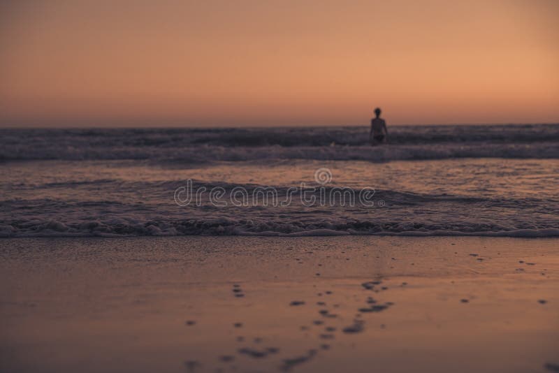 An Abandoned Beach with a Lone Swimmer on the Horizon at Sunset Stock ...