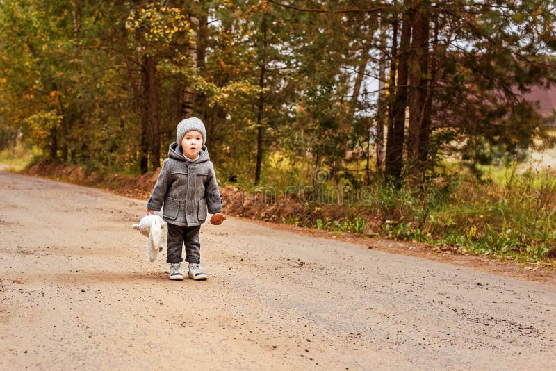 Lost child boy yelling halloo in the woods in a gray coat with a toy bunny and a mushroom in his hands