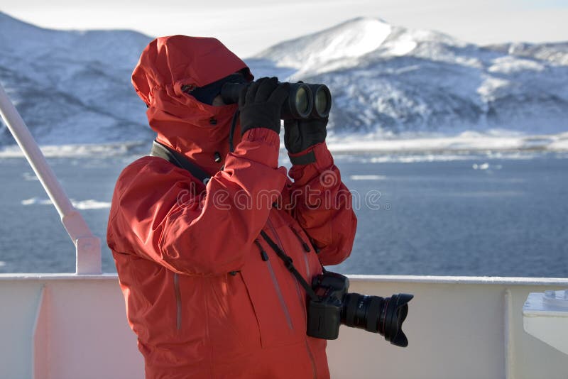 An adventure tourist looking through binoculars on a cruise ship in Antarctica. An adventure tourist looking through binoculars on a cruise ship in Antarctica