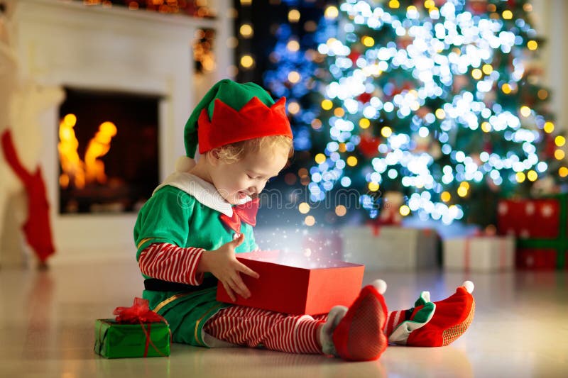 Abertura da criança atual na árvore de Natal em casa Criança no traje do duende com presentes e brinquedos do Xmas