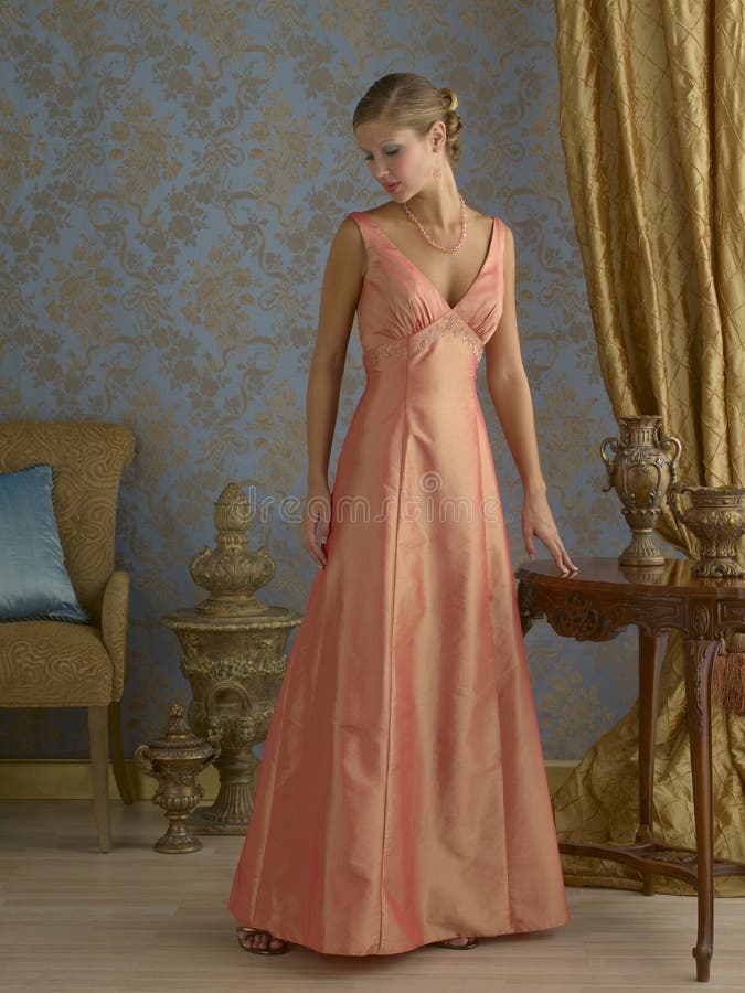 Beautiful blond fashion model wearing light orange evening gown in fancy room setting. Beautiful blond fashion model wearing light orange evening gown in fancy room setting.