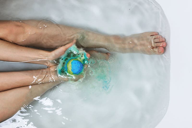 Above shot of woman`s legs and hands holding bath bomb in a tub