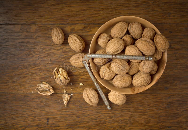 Above View of Walnuts grown in Oregon, in a Wooden Bowl on a Dark wood Table Background with some cracked and the nutcracker. It`s horizontal with room or space for copy, text, crop or your words