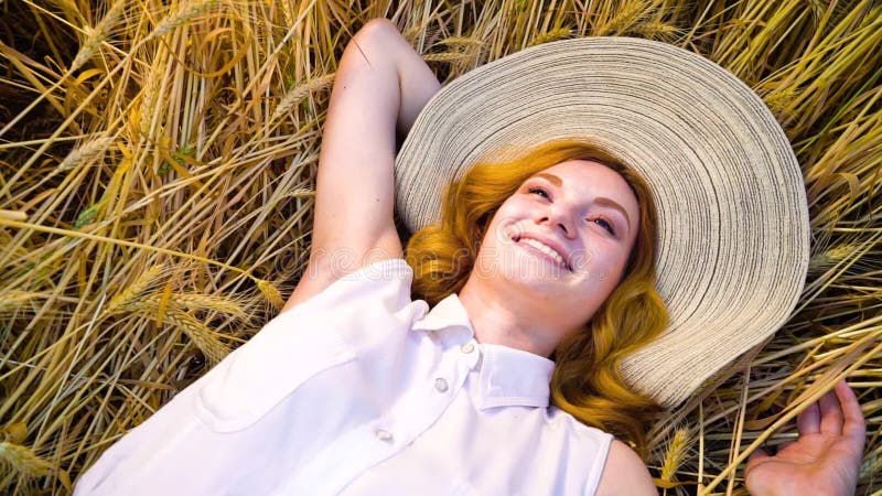 Above view young romantic red haired woman lying on wheat field and day dreaming