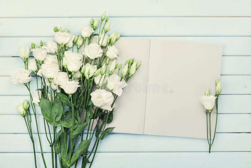 Abra el cuaderno y el ramo vacíos de eustoma de las flores blancas en la tabla rústica azul desde arriba Escritorio de trabajo de foto de archivo Abra el cuaderno y el ramo vacíos de eustoma de las flores blancas en la tabla rústica azul desde arriba Escritorio de trabajo de foto de archivo