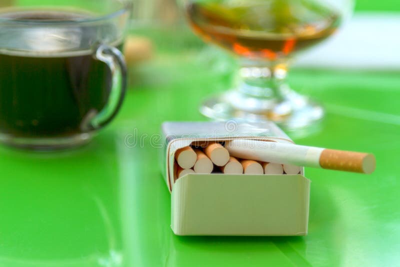 Open pack of cigarettes, Glass of Cognac brandy and a cup of coffee on a green table. Open pack of cigarettes, Glass of Cognac brandy and a cup of coffee on a green table