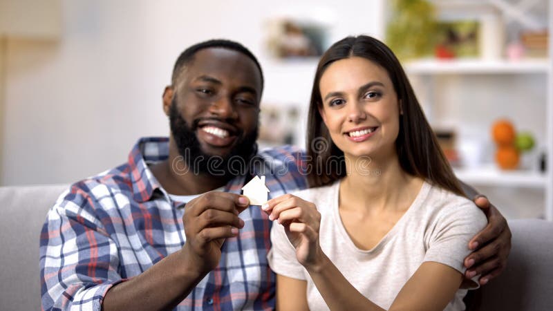 Abraçando a família multi-étnico que guarda a casa do papel, compra dos bens imobiliários, hipoteca fotografia de stock royalty free Abraçando a família multi-étnico que guarda a casa do papel, compra dos bens imobiliários, hipoteca fotografia de stock royalty free