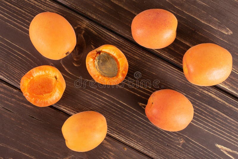 Abricot orange frais sur le bois brun. Groupe de cinq totalités deux moitiés d'abricot orange profond frais avec une pierre flatlay sur le bois brun