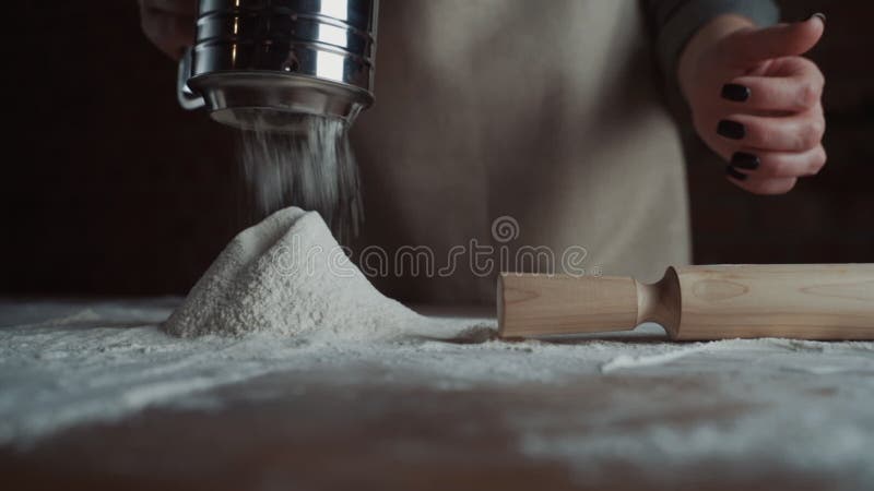 Abschluss den Frauenbäckereichef, der Mehl vom Sieb auf dem Tisch bereit für die Herstellung von hausgemachten Brot siebt. Zeitlup