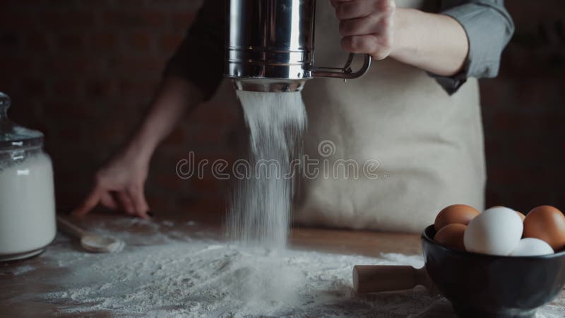 Abschluss den Frauenbäckereichef, der Mehl vom Sieb auf dem Tisch, bereitend für die Herstellung von hausgemachten Brot siebt vor