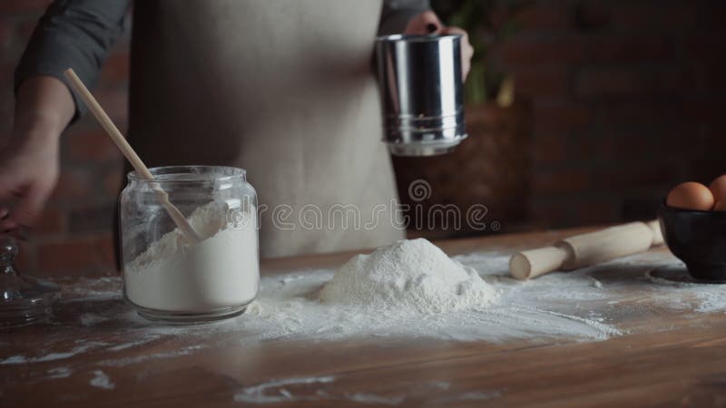 Abschluss den Frauenbäckereichef, der Mehl vom Sieb auf dem Tisch, bereitend für die Herstellung von hausgemachten Brot siebt vor