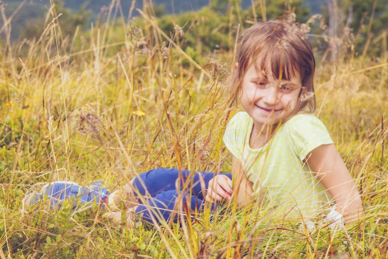 Abschluss in nette Kindermädchenlüge auf einer Wiese im Gras gegen Gebirgshintergrund. Frohe Kind haben einen Rest in den Bergen. lizenzfreie stockfotos