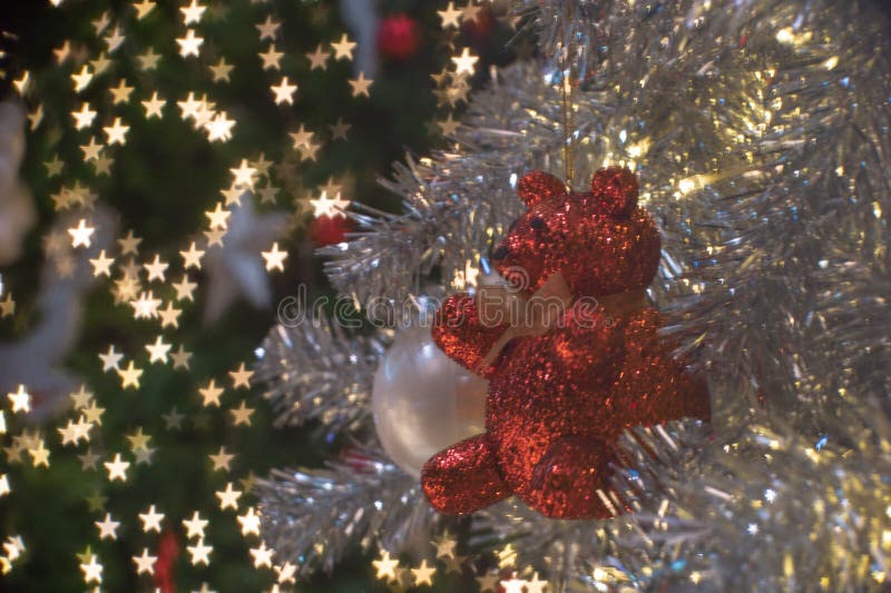 Abstract background of glittering bokeh lights in little star shape with blurred ornament on the silver Christmas tree in foreground. Abstract background of glittering bokeh lights in little star shape with blurred ornament on the silver Christmas tree in foreground