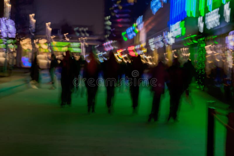 Abstract background. Intentional motion blur. Group of young people going along the street. Green shop window