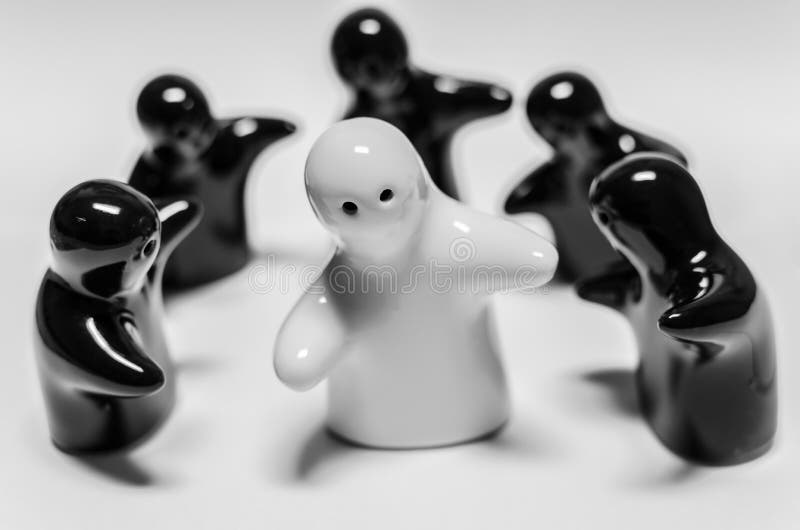 Abstract image of white ceramic doll standing among black ceramic dolls stock photography