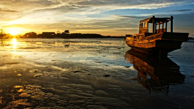 Astratto paesaggio di mare, il tramonto, la marea di uscire, sole, raggio di sole brillare sul peschereccio di legno che relfect sulle acque di superficie di spiaggia, colorato, cielo, sera di scena.