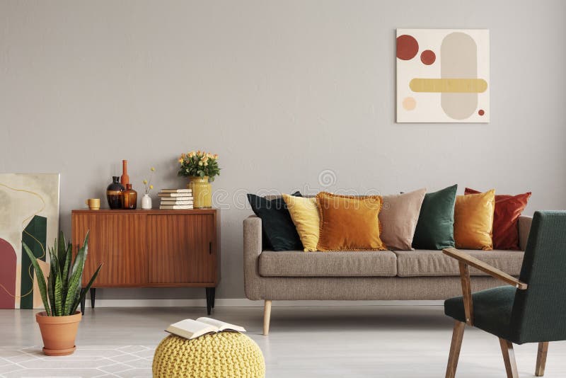 Abstract painting on grey wall of retro living room interior with beige sofa with pillows, vintage dark green armchair and yellow