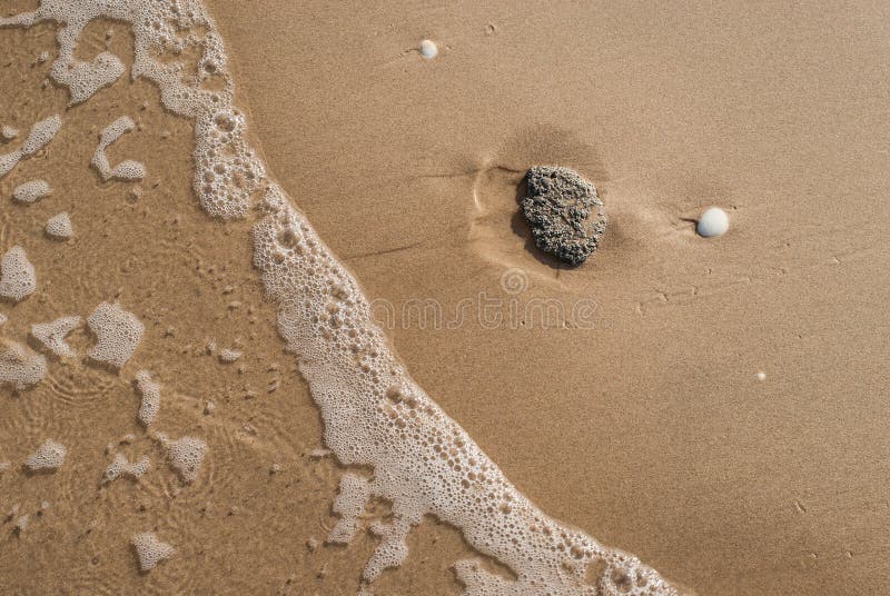 Abstract sand background with lying stone and bubbling ocean water