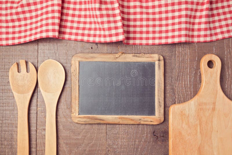 Abstract wooden background with red checked tablecloth, chalkboard and kitchen utensils. View from above