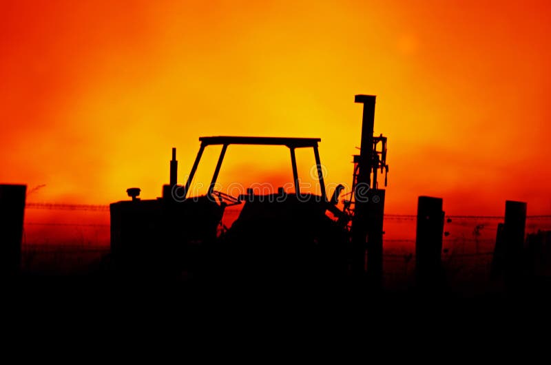 An abstract background showing the silhouette image of a farm barb wire fence and tractor set against the red orange background of the flames blazing away in a terrible Australian bushfire. An abstract background showing the silhouette image of a farm barb wire fence and tractor set against the red orange background of the flames blazing away in a terrible Australian bushfire.