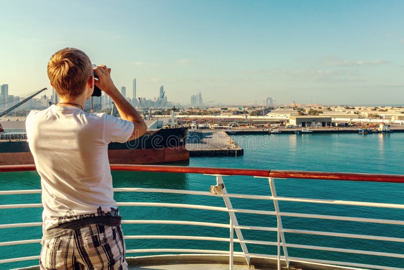 Abu Dhabi Zjednoczone Emiraty Arabskie, Grudzień, - 13, 2018: Młody człowiek patrzeje przez lornetek od rejsu liniowa miasto na obraz stock Abu Dhabi Zjednoczone Emiraty Arabskie, Grudzień, - 13, 2018: Młody człowiek patrzeje przez lornetek od rejsu liniowa miasto na obraz stock