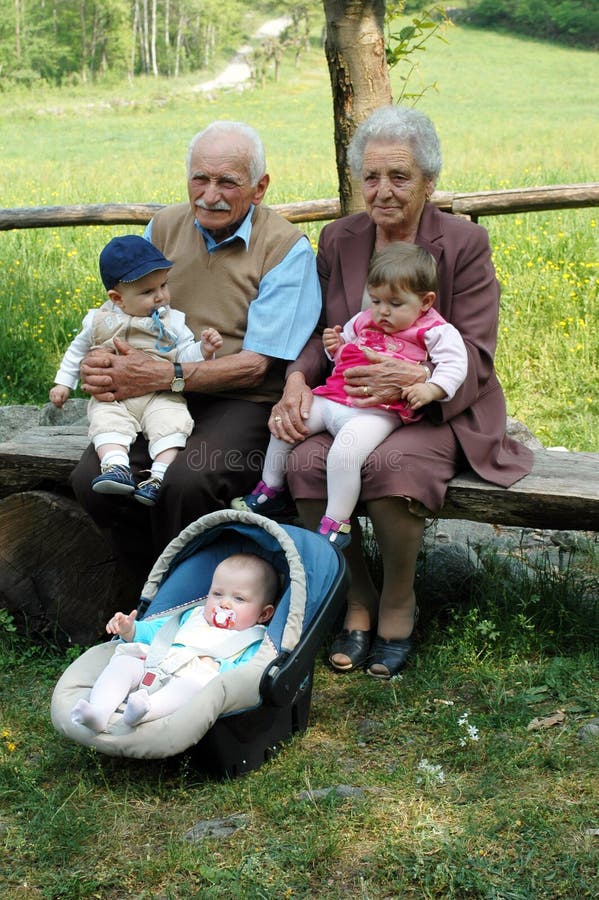 Grandparents with three grandchildren sitting on a bench in a park during a family reunion. Grandparents with three grandchildren sitting on a bench in a park during a family reunion