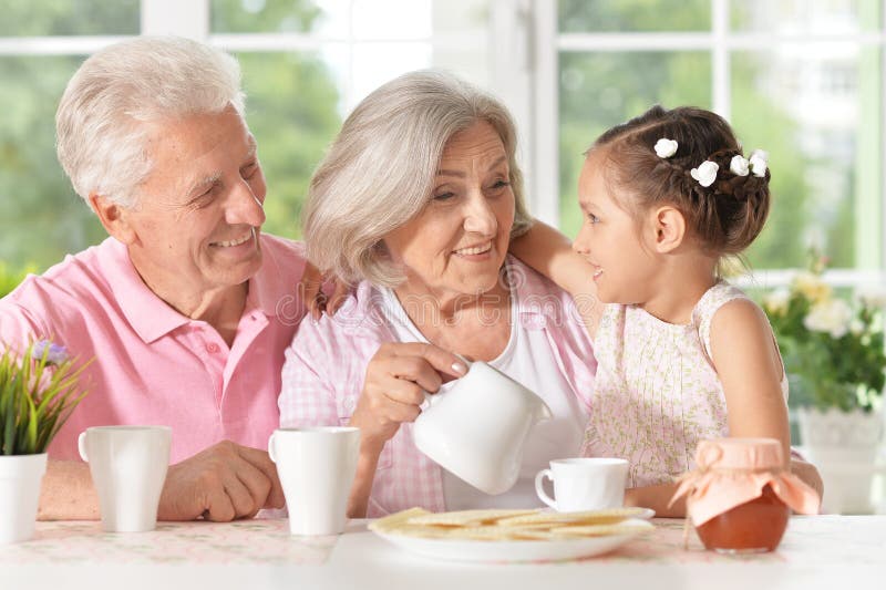 Abuelos con té de consumición de la nieta imagen de archivo Abuelos con té de consumición de la nieta imagen de archivo