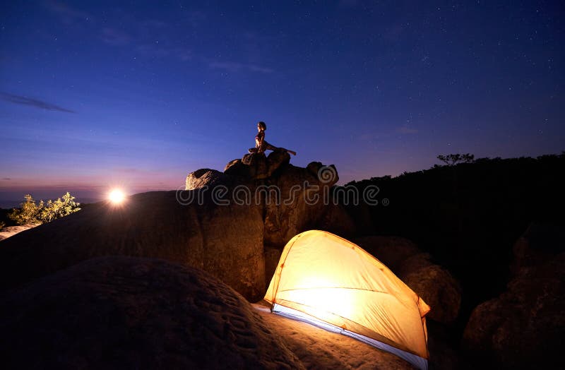 Acampamento na noite na formação de rocha Barraca e mulher do turista que fazem a ioga na parte superior da montanha foto de stock Acampamento na noite na formação de rocha Barraca e mulher do turista que fazem a ioga na parte superior da montanha foto de stock