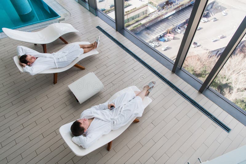 Accappatoio d'uso del giovane due, trovantesi sulla chaise-lounge nel salone della stazione termale e parlante l'un l'altro davan fotografia stock Accappatoio d'uso del giovane due, trovantesi sulla chaise-lounge nel salone della stazione termale e parlante l'un l'altro davan fotografia stock