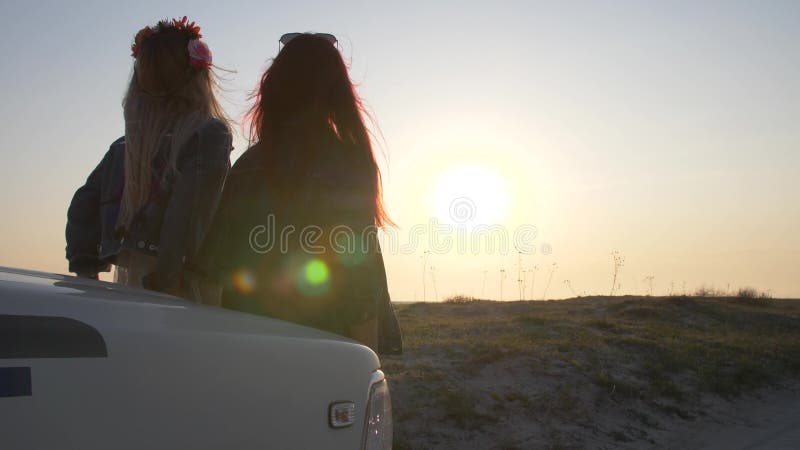 Accoppi delle giovani donne sta sedendosi sul paraurti e godono del tramonto