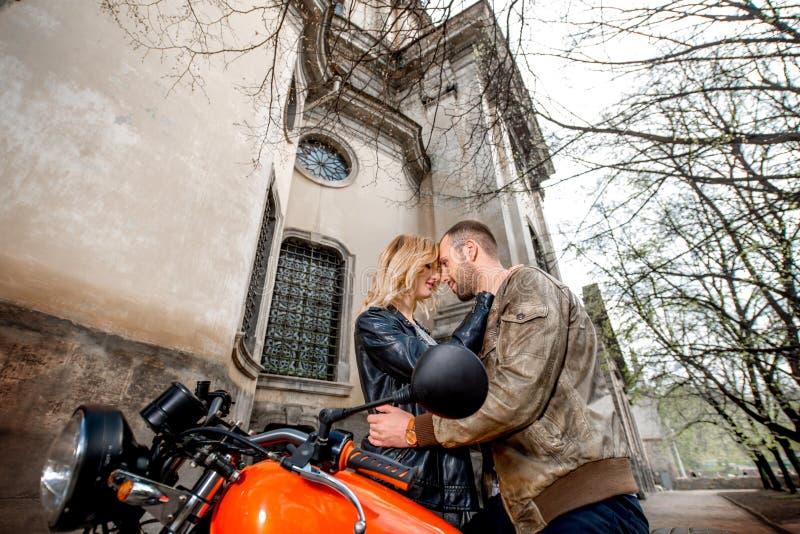 Accoppi l'abbraccio vicino al motociclo sui vecchi precedenti della città immagine stock Accoppi l'abbraccio vicino al motociclo sui vecchi precedenti della città immagine stock
