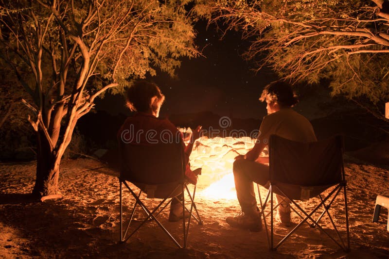 Accoppi la seduta al fuoco bruciante del campo nella notte Accampandosi nella foresta sotto il cielo stellato, la Namibia, Africa immagini stock libere da diritti Accoppi la seduta al fuoco bruciante del campo nella notte Accampandosi nella foresta sotto il cielo stellato, la Namibia, Africa immagini stock libere da diritti