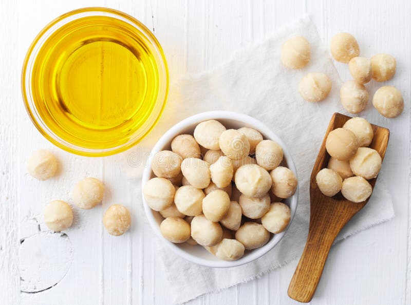 Bowl of macadamia nut oil and macadamia nuts on white wooden background. From top view. Bowl of macadamia nut oil and macadamia nuts on white wooden background. From top view