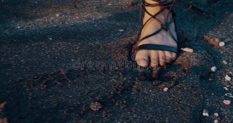 Acercar las piernas femeninas caminando en la playa de arena negra con conchas marinas