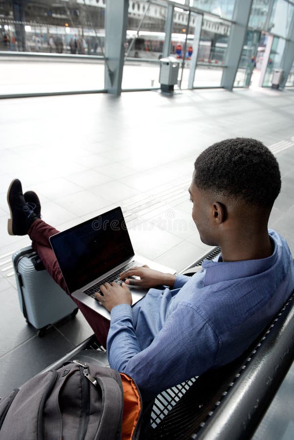 Achter van het Afrikaanse Amerikaanse reizende zakenman wachten op bank met zakken en laptop stock foto Achter van het Afrikaanse Amerikaanse reizende zakenman wachten op bank met zakken en laptop stock foto