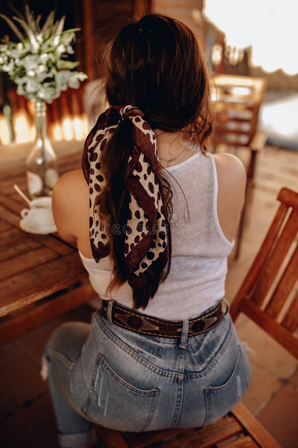 Achteraanzicht van een sexy jonge brunette vrouw met een paardenstaart en een banaan die op haar rug op een terras zit en een kop royalty-vrije stock foto's Achteraanzicht van een sexy jonge brunette vrouw met een paardenstaart en een banaan die op haar rug op een terras zit en een kop royalty-vrije stock foto's